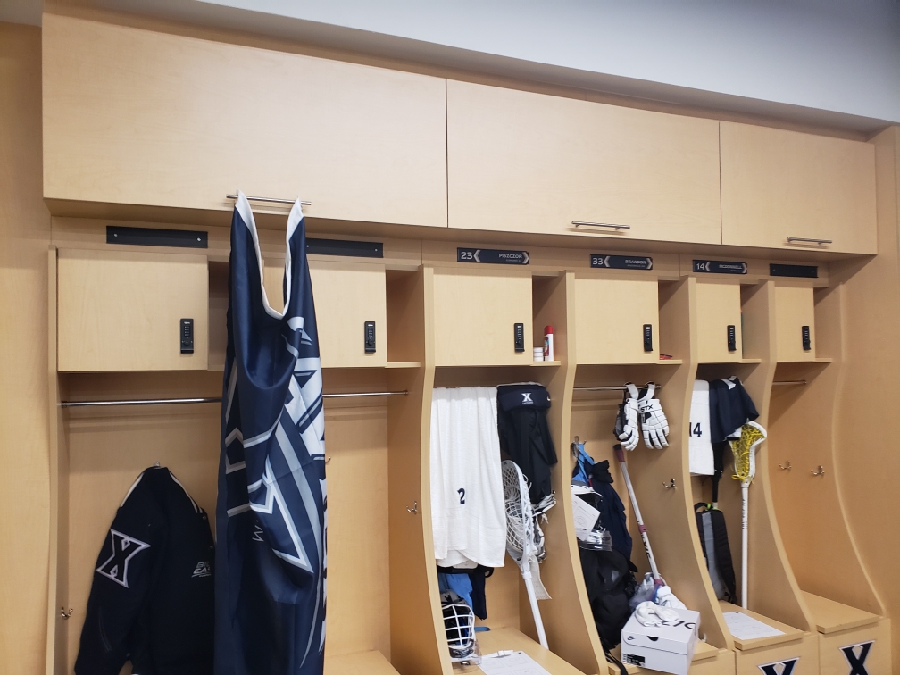 Xavier University lacrosse locker room with battery powered locks with overhead storage and bench seating storage