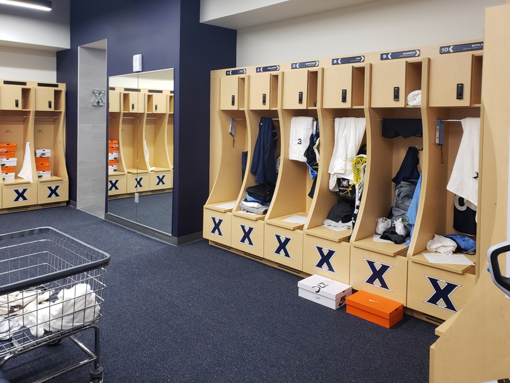 Xavier University lacrosse locker room with battery powered locks with overhead storage and bench seating storage and custom laminate graphics
